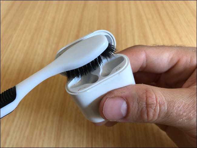 Mano sosteniendo un estuche de Apple AirPods y limpiándolo con un cepillo de dientes.