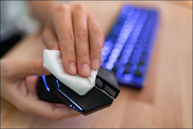Una mano limpiando un mouse de computadora con un paño.