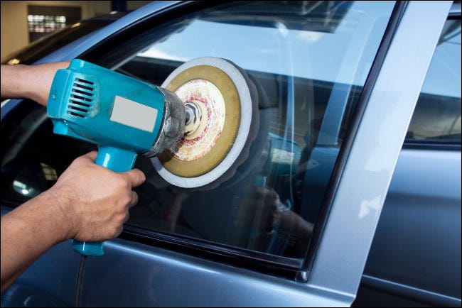 Las manos de un hombre pulen la ventanilla de un automóvil con una máquina de almohadilla eléctrica.