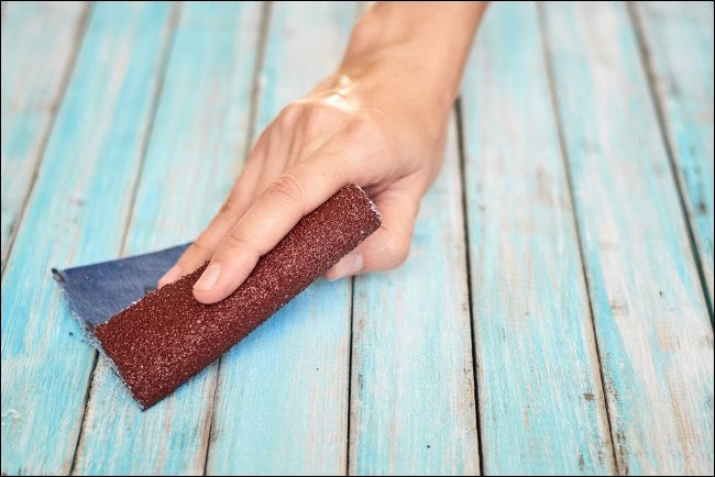 Lijar una madera a mano con un trozo de papel de lija.