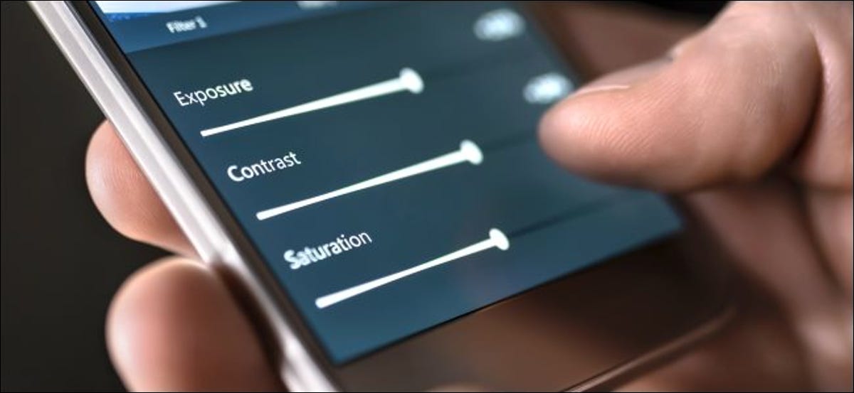 Alguien se esta ajustando "Exposición," "Contraste," y "Saturación" cursores en un teléfono inteligente.