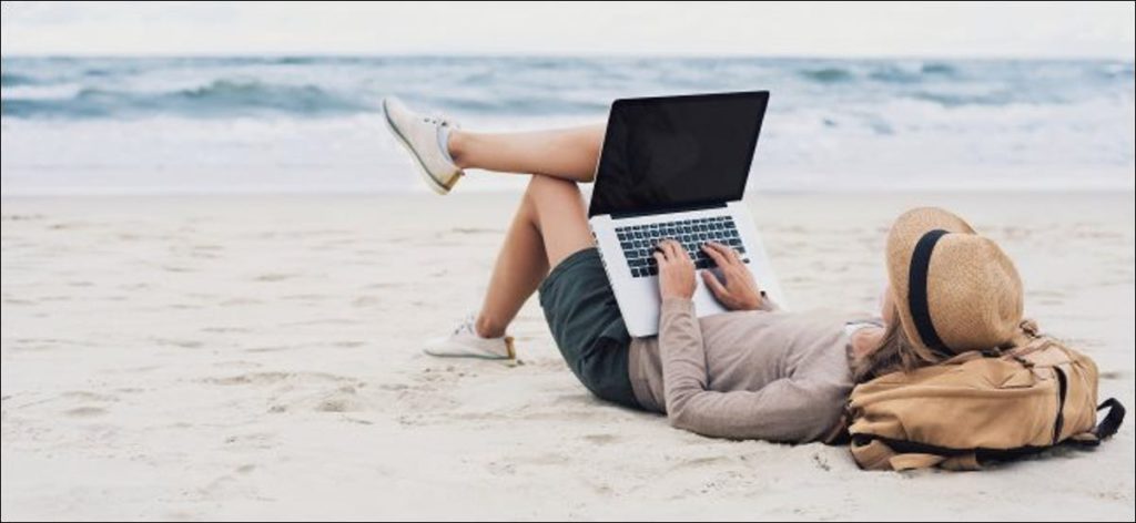 Una mujer que usa una computadora portátil mientras está acostada en una playa.