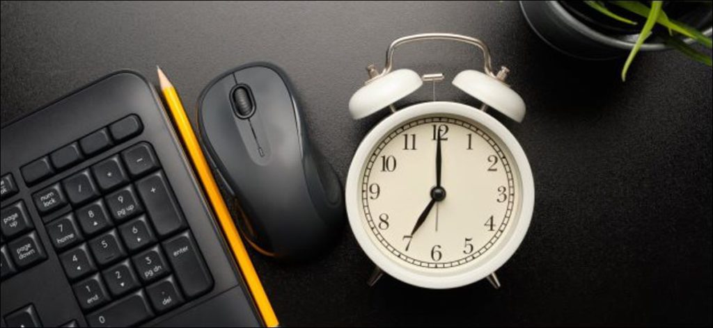 Un reloj de alarma junto a un teclado y un mouse de computadora.