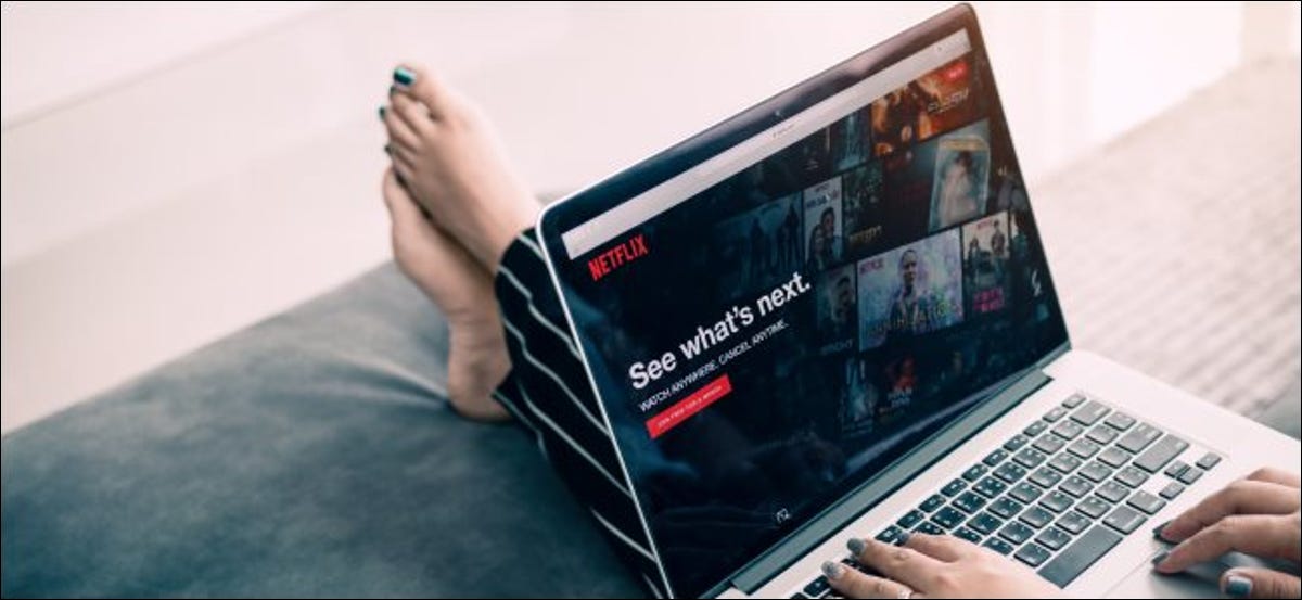 Los pies de una mujer se estiran sobre un reposapiés mientras navega por Netflix en una computadora portátil.