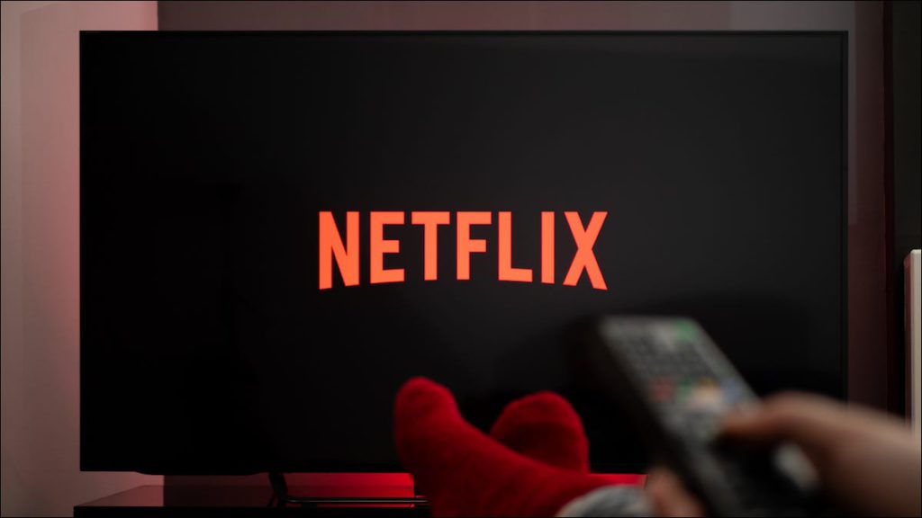 Logotipo de Netflix en un televisor inteligente y una persona que sostiene un control remoto