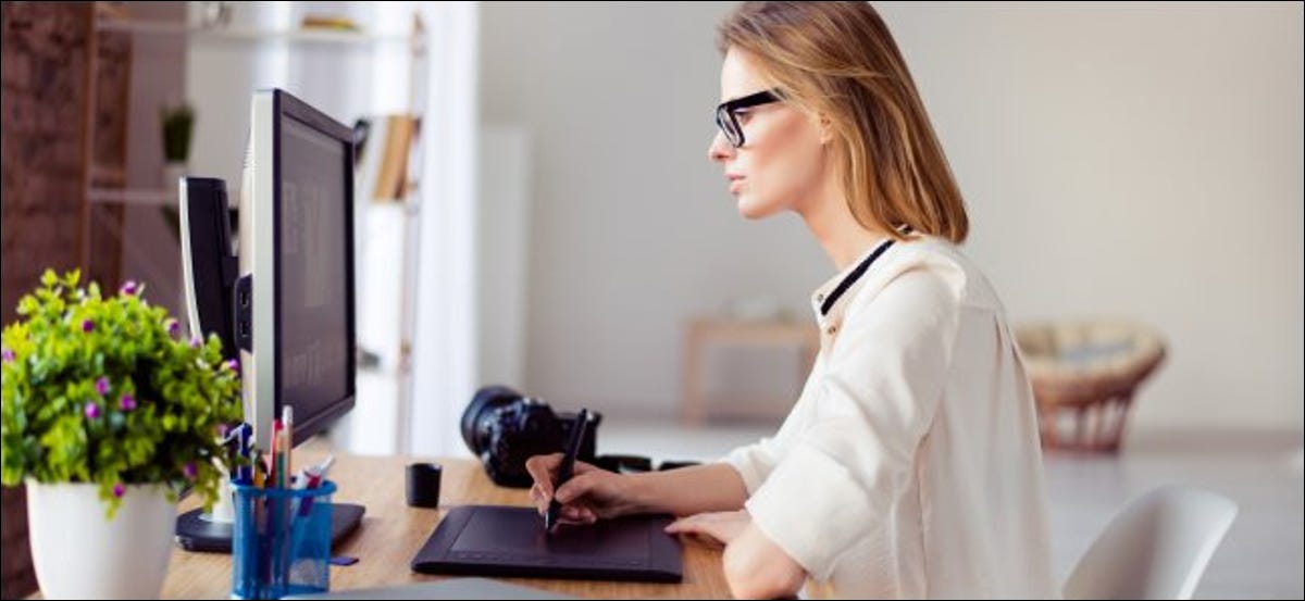 Una mujer que trabaja con una tableta gráfica frente a una computadora.