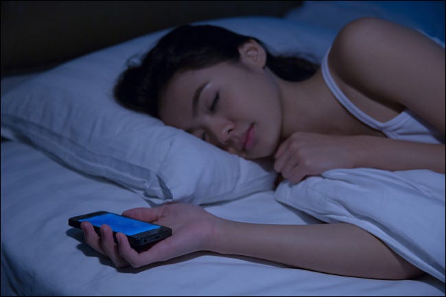 Una mujer durmiendo sosteniendo un teléfono inteligente.