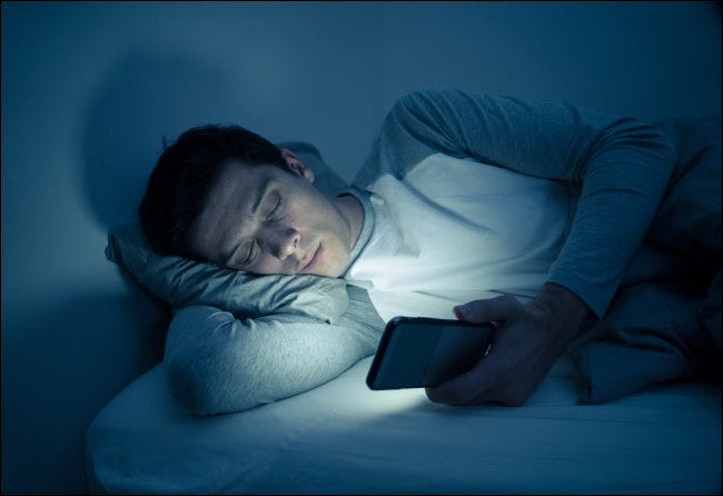 Un hombre está enviando mensajes de texto en su teléfono inteligente en la cama por la noche.