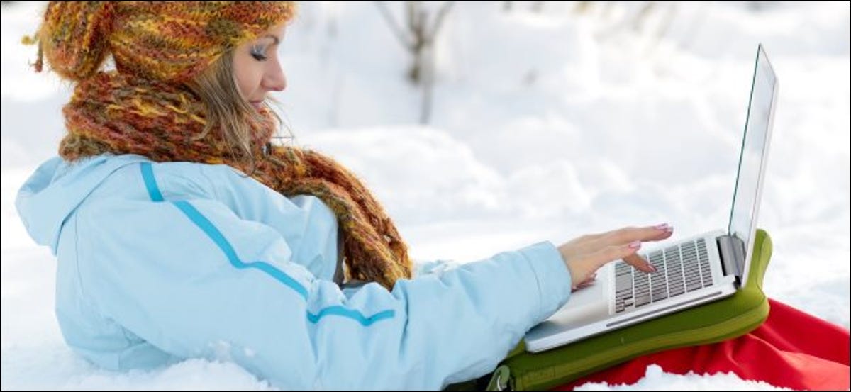 Una mujer que usa un MacBook al aire libre en la nieve.