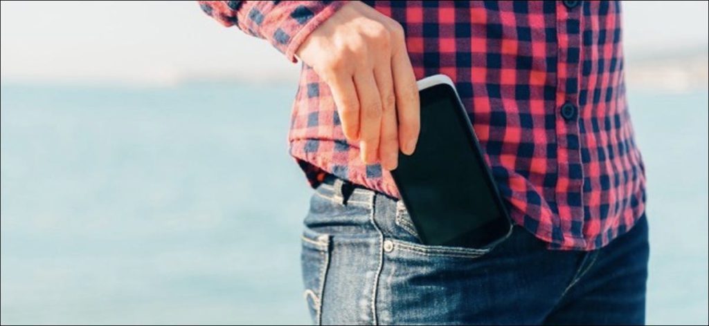 Una mujer saca su teléfono celular del bolsillo de sus jeans en la playa cerca del mar para tomar un autorretrato o fotografiar el mar