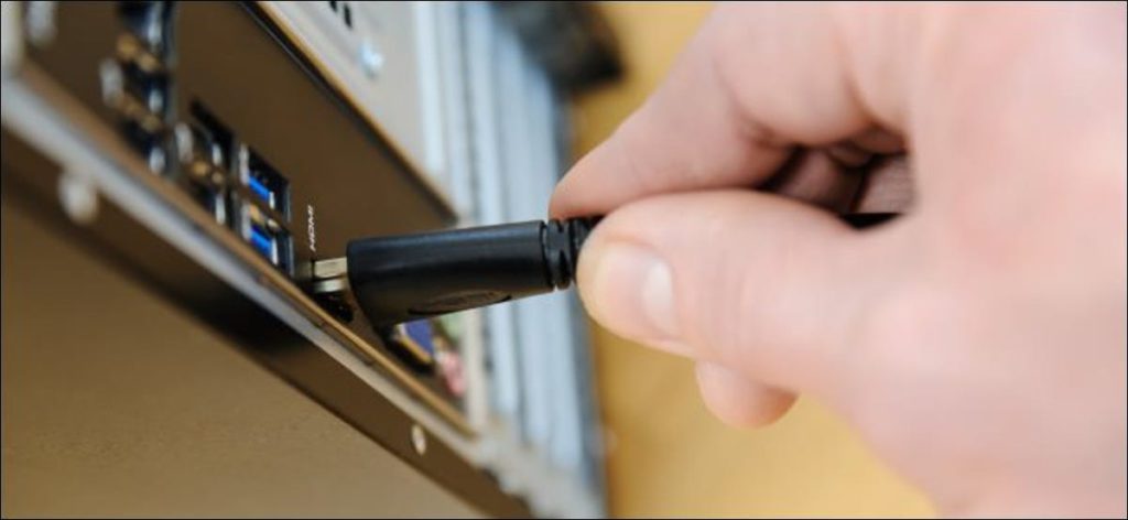 Una mano conectando un cable HDMI a una computadora de escritorio.