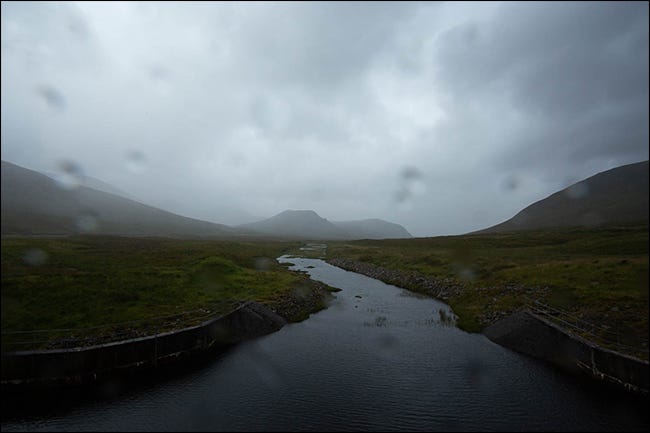 Una foto lluviosa de una montaña y un arroyo con gotas de agua en la lente. 