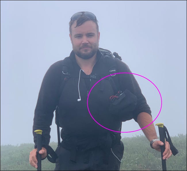 Un hombre que camina bajo la lluvia con un trípode y una bolsa Peak Design Camera Shell.