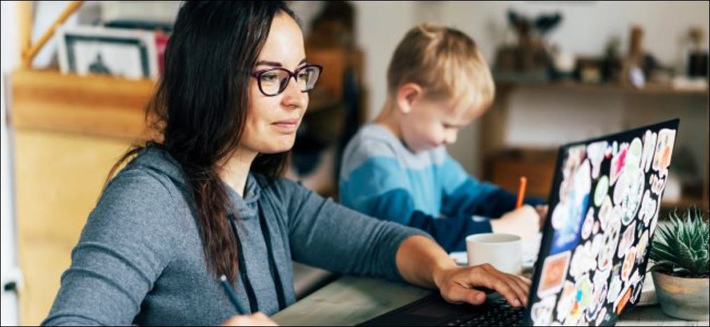 Una mujer que trabaja en una computadora portátil con un niño sentado junto a su dibujo.