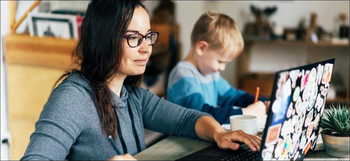 Una mujer que trabaja en una computadora portátil con un niño sentado junto a su dibujo.