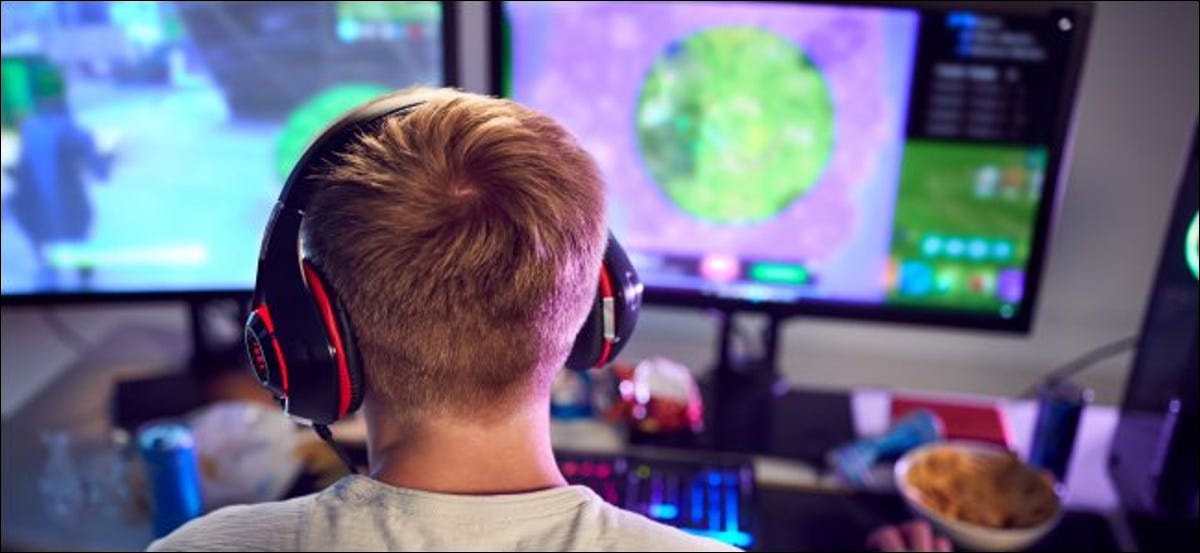 La espalda de un niño, que usa audífonos y está sentado frente a una computadora con dos pantallas.