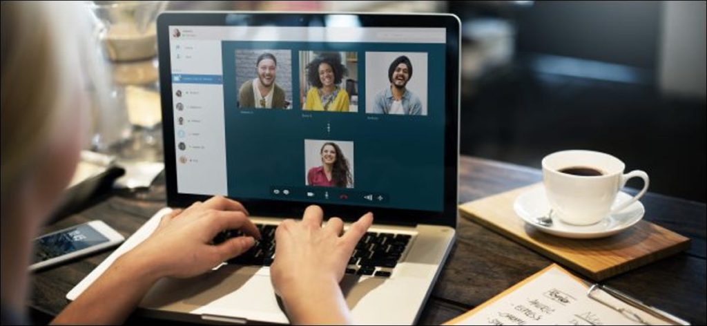 Las manos de una mujer en el teclado de su computadora portátil, con videoconferencia de cuatro personas en la pantalla.