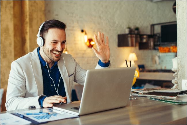 Un hombre con auriculares y saludando a su computadora portátil.