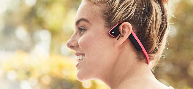 Mujer con auriculares de conducción ósea AfterShokz.  Parece que se está divirtiendo, pero podría molestar a un transeúnte.