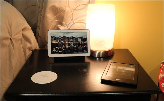 Una mesita de noche con un cargador inalámbrico integrado en la superficie, un Kindle y Google Home Hub