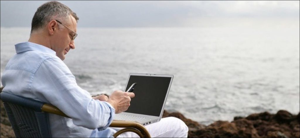 Retrato de un hombre sentado con un portátil frente al mar