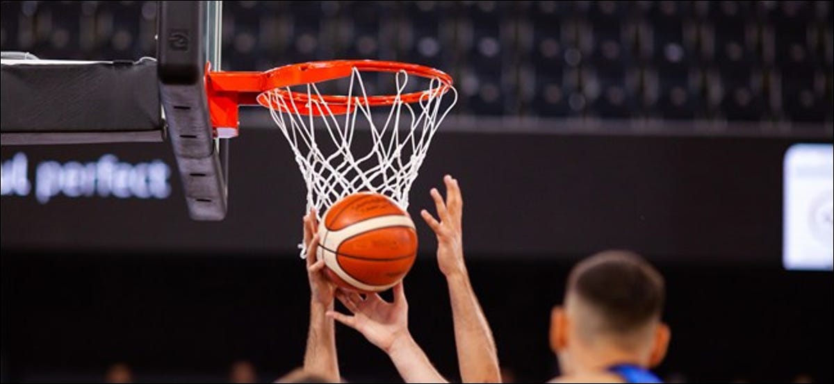 Manos alcanzando una pelota de baloncesto frente a la red.