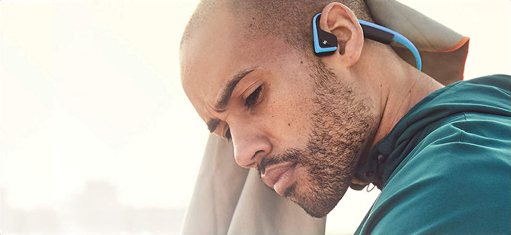 Hombre con auriculares de conducción ósea AfterShokz.  Se ve muy pensativo.  Quizás esté escuchando un podcast.