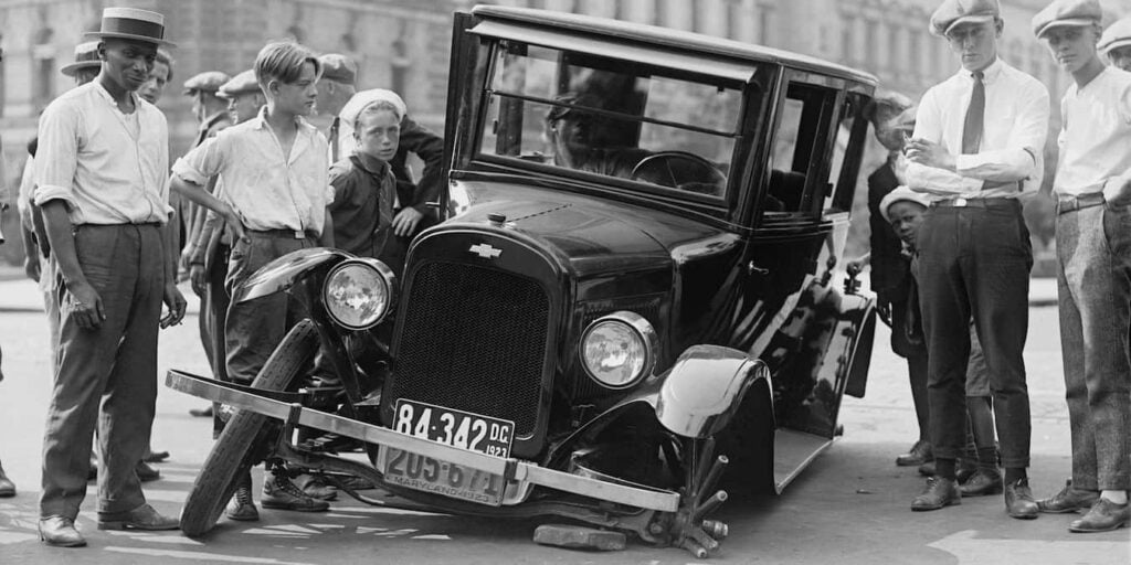 A broken car surrounded by people.